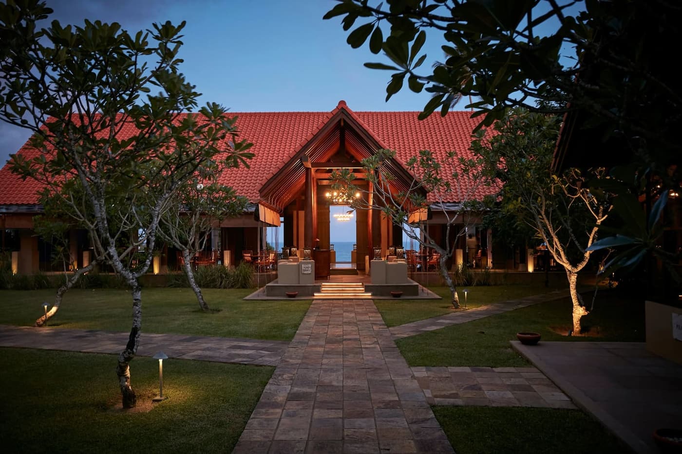 A pavilion with a red tiled roof, lit at dusk across a lawn