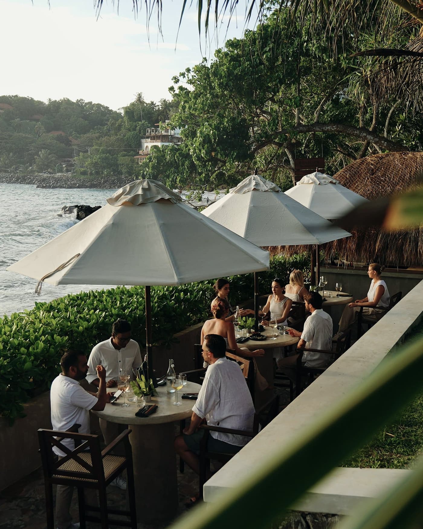 Friends at a long lunch under white parasols in a garden