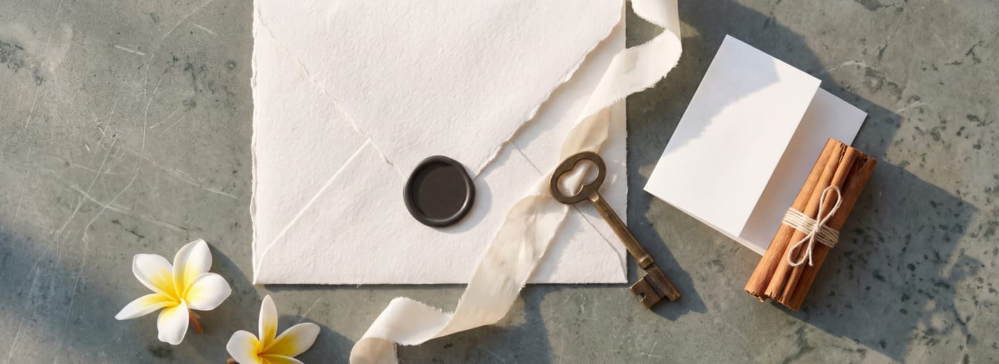 A sealed invitation on stone with a ribbon, a key and frangipani
