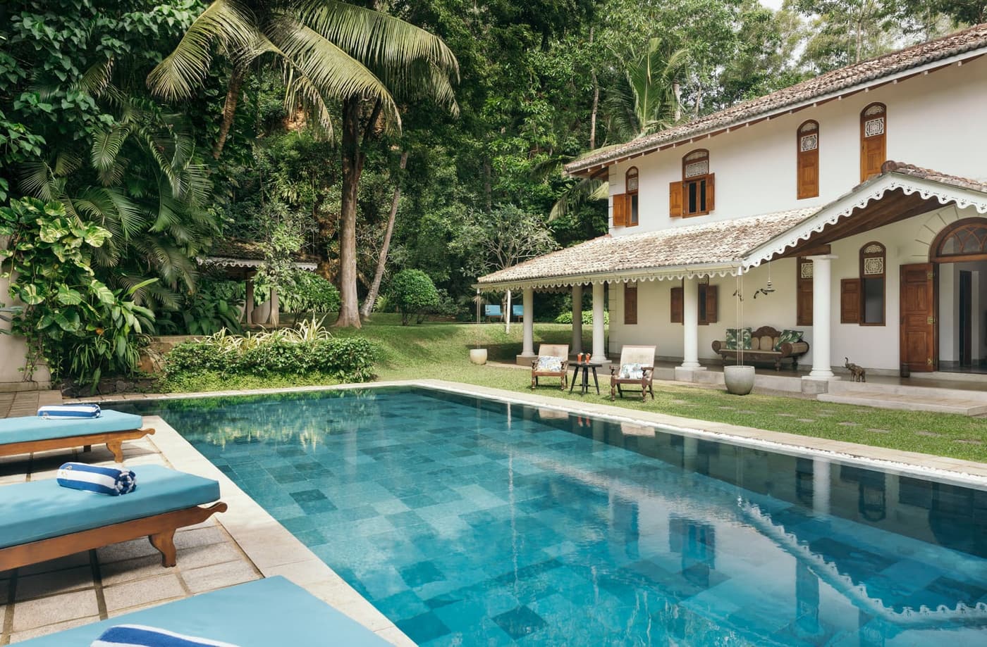 A white colonial villa behind a long blue pool