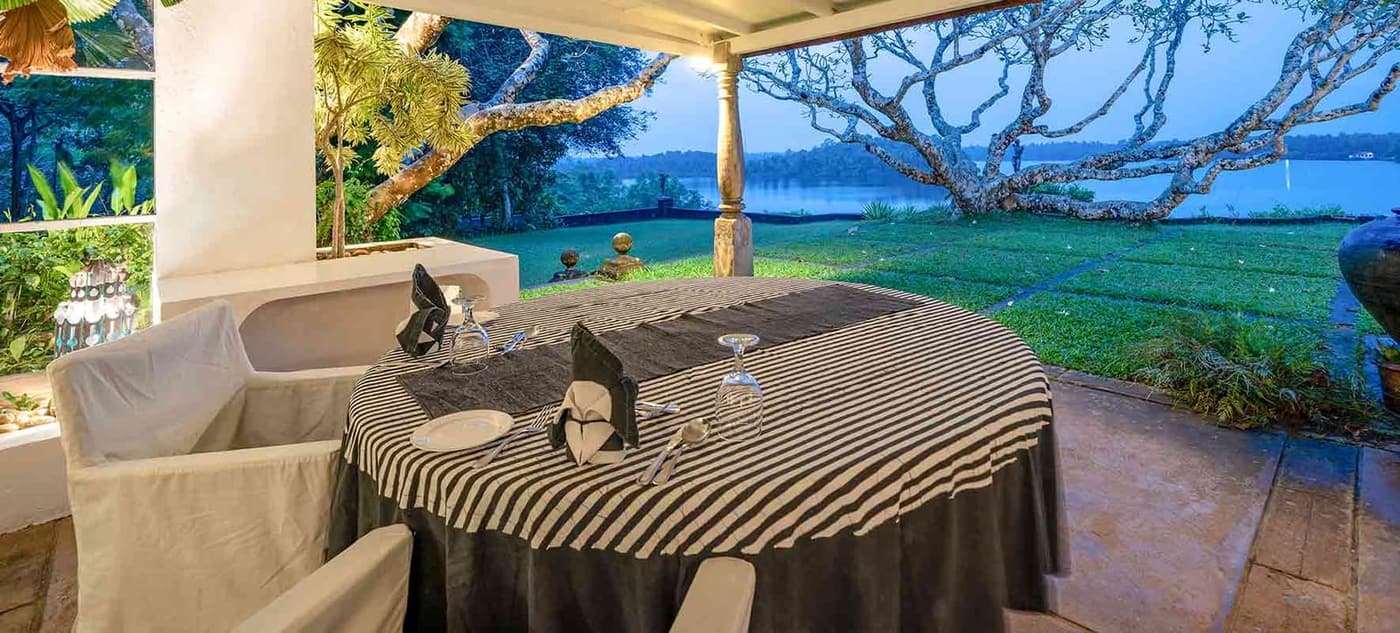 A table laid under a frangipani tree above a lake