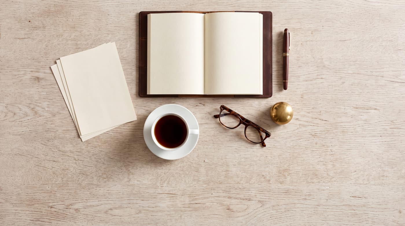 An open notebook, loose pages, glasses and a cup of coffee