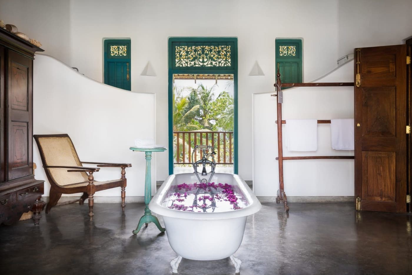 A bath strewn with flowers beside tall shuttered windows